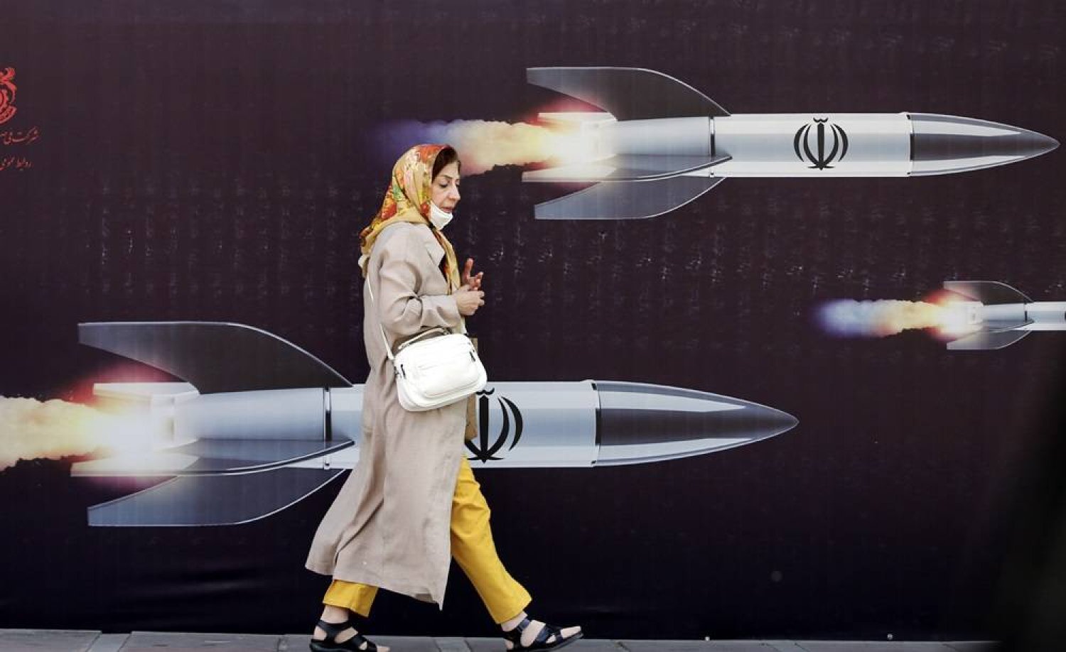 An Iranian woman walks past a huge anti-Israeli banner carrying pictures of missiles, in Tehran, Iran, 19 April 2024. (EPA)