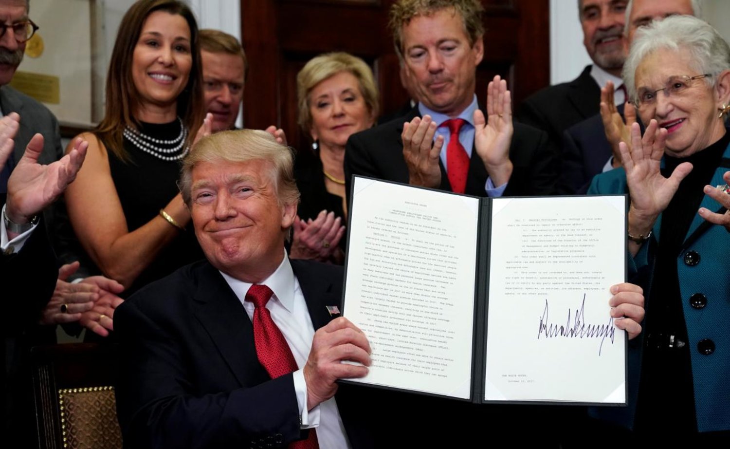 President Trump smiles after signing an Executive Order to make it easier for Americans to buy bare-bone health insurance plans and circumvent Obamacare, Reuters 