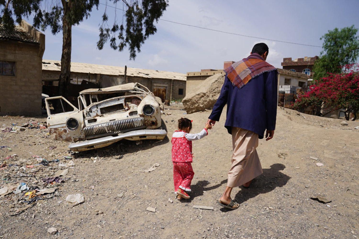 In the Harat Al-Masna’a slum in Sana’a, Yemen, a man walks with his three-year-old daughter which sits next to a former textile factory and hosts 231 families of former factory workers. Photo: Giles Clarke for UNOCHA