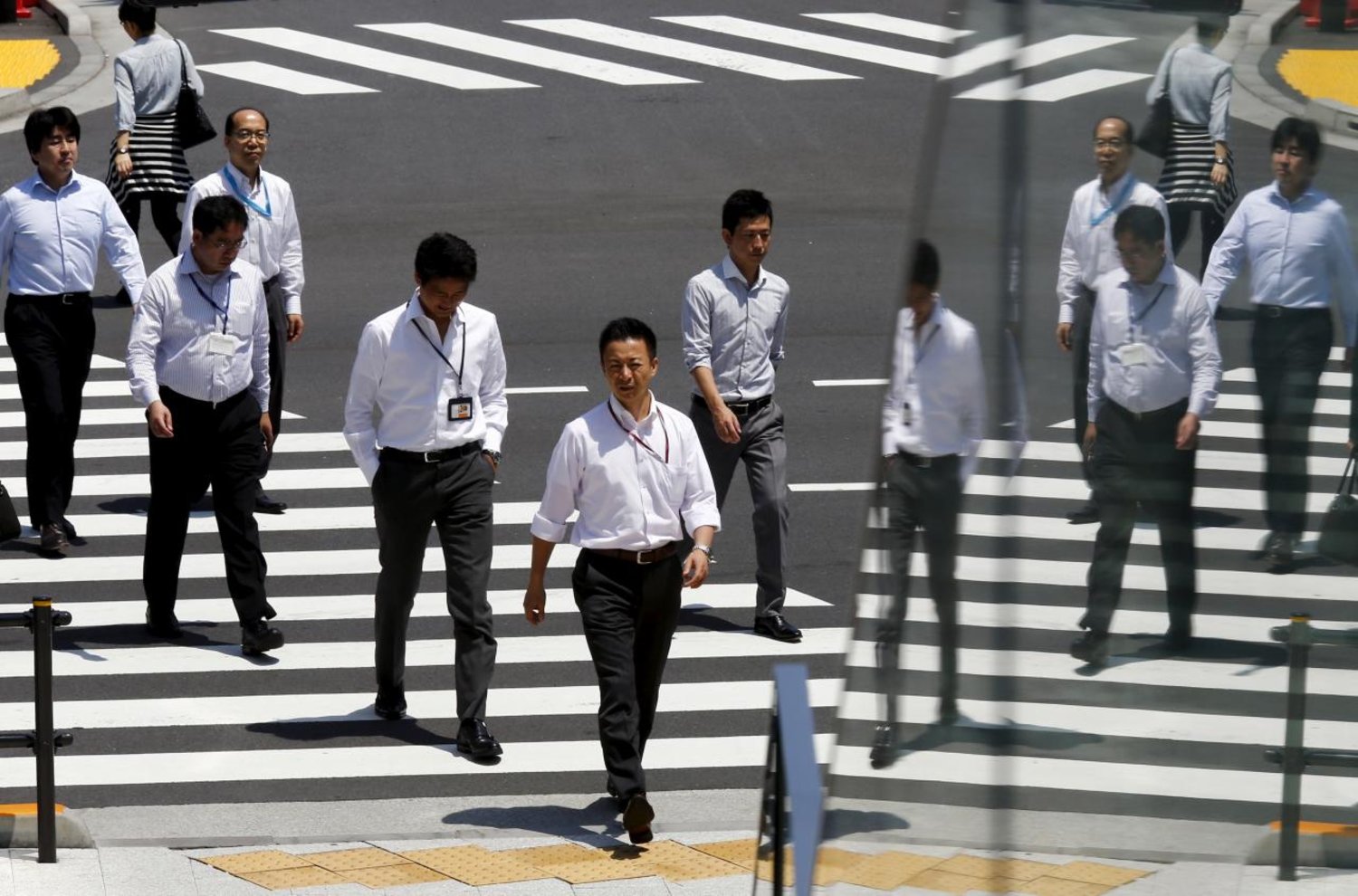 Office workers are reflected in a glass railing as they cross a street during lunch hour in Tokyo June 1, 2015. REUTERS/Thomas Peter/File Photo
