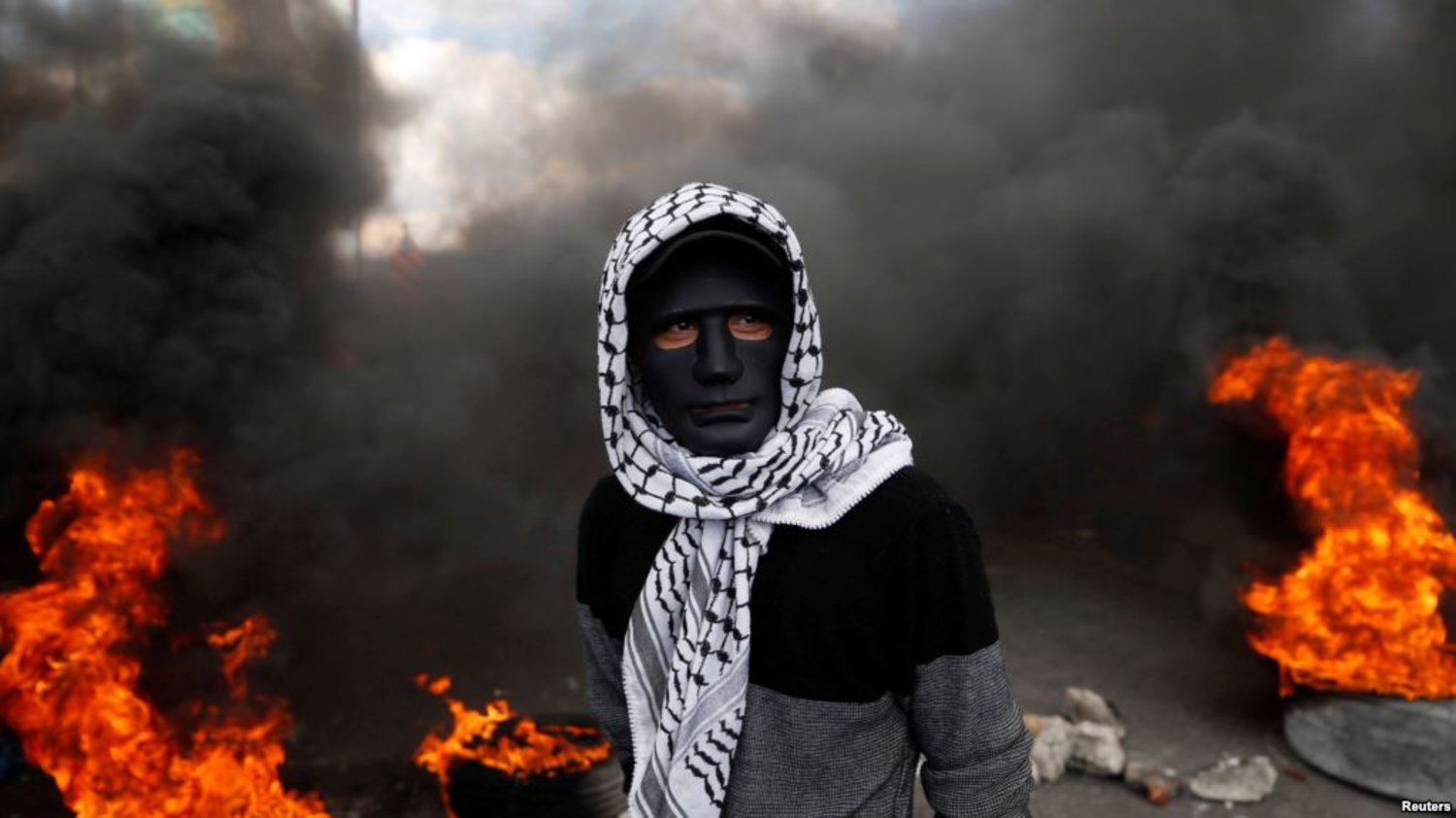 A Palestinian demonstrator stands near burning tires during clashes with Israeli troops. - Reuters 