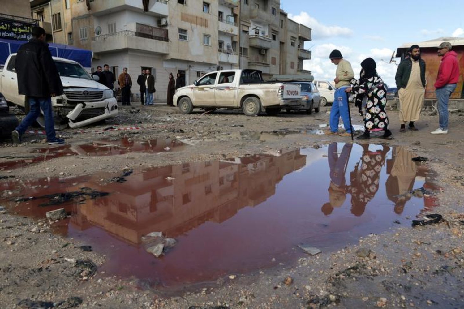People walk near a puddle of water mixed with blood at the site of twin car bombs in Benghazi that resulted in scores of deaths and injuries, Libya, January 24, 2018. (Reuters)