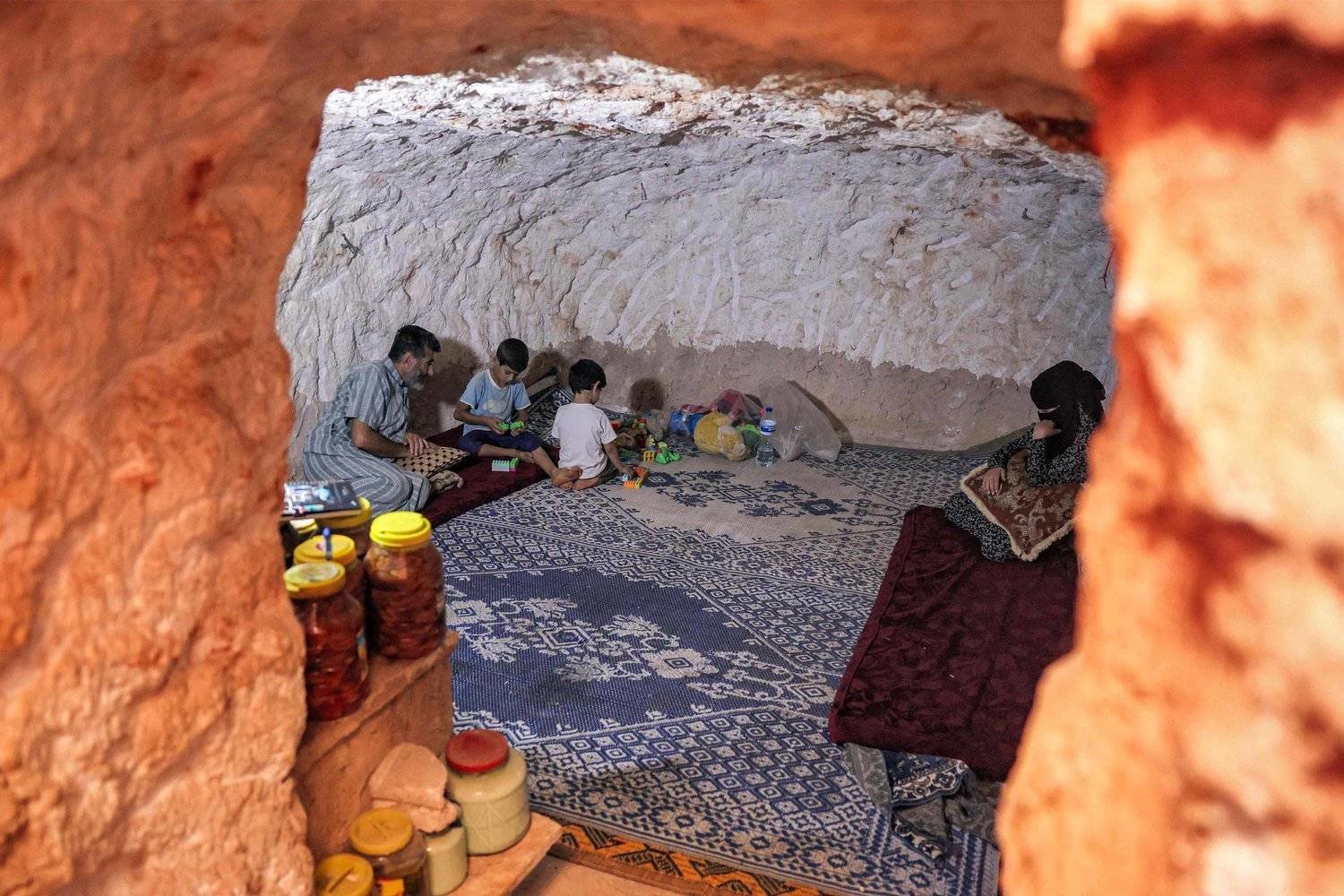 Ahmad Khalil, 53, sits with his family in a cave he carved manually with his children in five years, near his original home in the mostly abandoned village of Kansafra, on September 10, 2023. (Photo by Omar HAJ KADOUR / AFP)