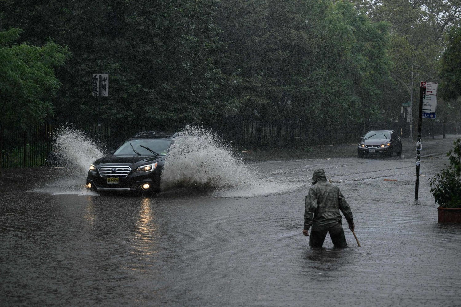 A man clears debris from a drain as a car make their way through floodwater in Brooklyn, New York on September 29, 2023. (Photo by Ed JONES / AFP)