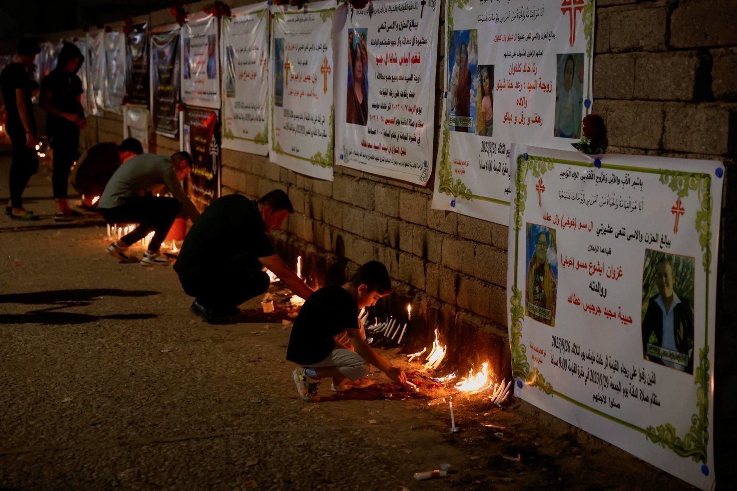 People light candles in front of pictures of some victims of the wedding hall fire in Al-Hamdaniya. (Reuters)