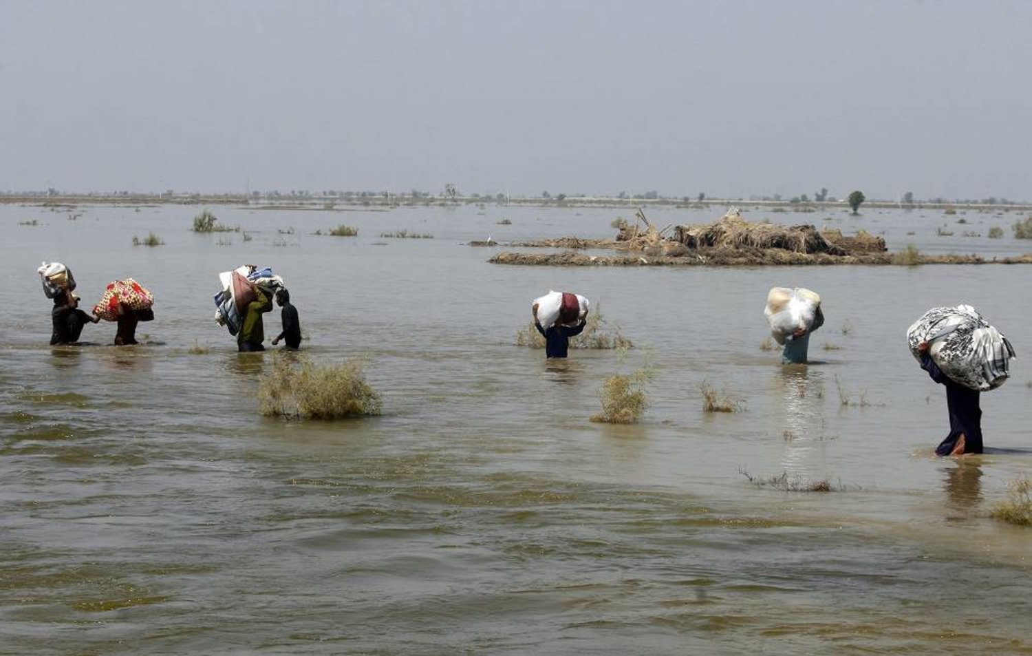 Victims of heavy flooding from monsoon rains carry relief aid through flood water in the Qambar Shahdadkot district of Sindh Province, Pakistan, Sept. 9, 2022. (AP)
