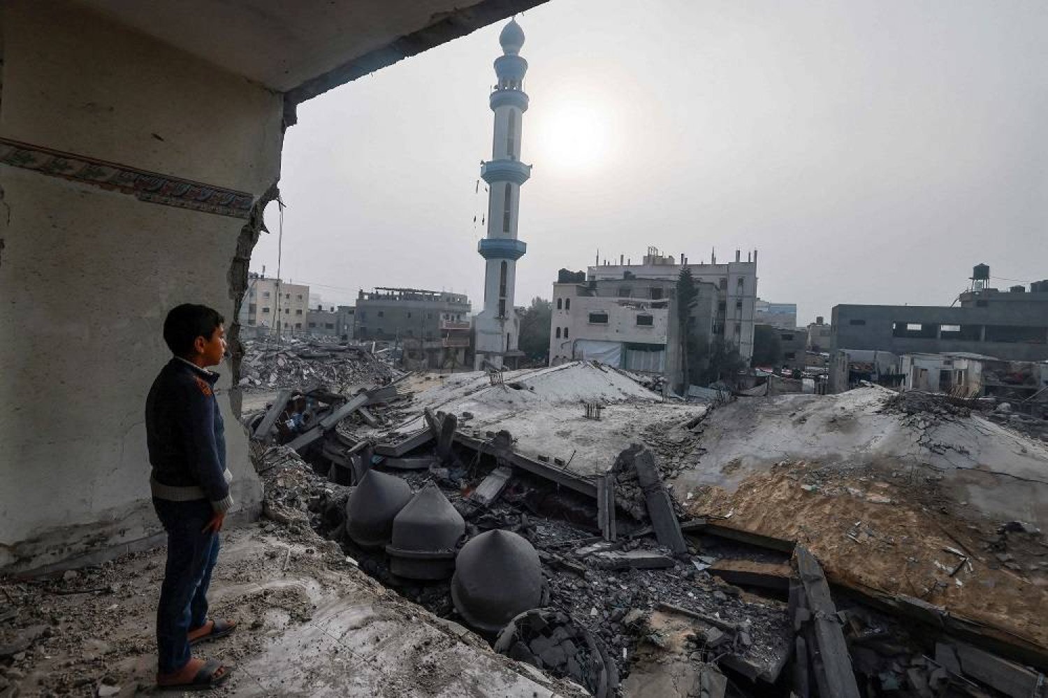 A child standing inside a damaged building, stares at the Al-Faruq mosque, levelled by Israeli bombardment in Rafah in the southern Gaza Strip on a foggy day on February 25, 2024, amid continuing battles between Israel and the Palestinian militant group Hamas. (AFP)
