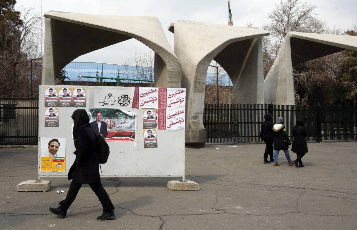 An Iranian student walks past election posters at the entrance of Tehran University. (EPA) 