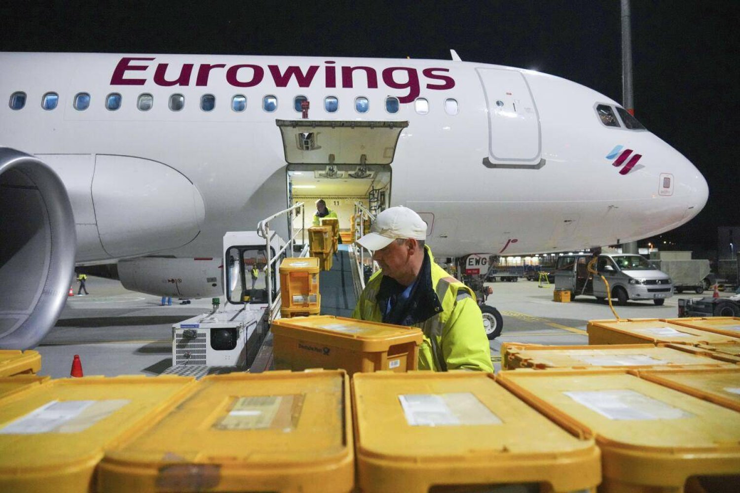 WISAG employees load a Eurowings Airbus A320-214 bound for Stuttgart with plastic boxes full of mail, at Berlin Brandenburg Airport, in Schönefeld, Germany, Thursday, March 28, 2024. (Soeren Stache/dpa via AP)