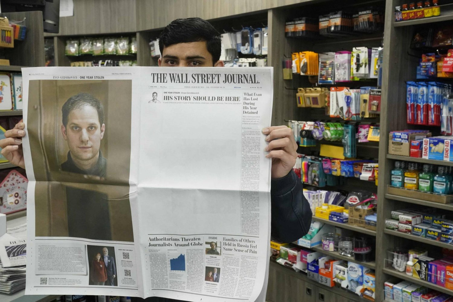 A New York City vendor poses with a March 29, 2024, copy of The Wall Street Journal showing a mostly blank front page to mark the one year anniversary of the imprisonment in Russia of their reporter Evan Gershkovich (portrait L.). Gershkovich was arrested in Russia on espionage charges and his family vowed March 29 to continue fighting for his release, a pledge echoed by US President Joe Biden. (Photo by TIMOTHY A. CLARY / AFP)