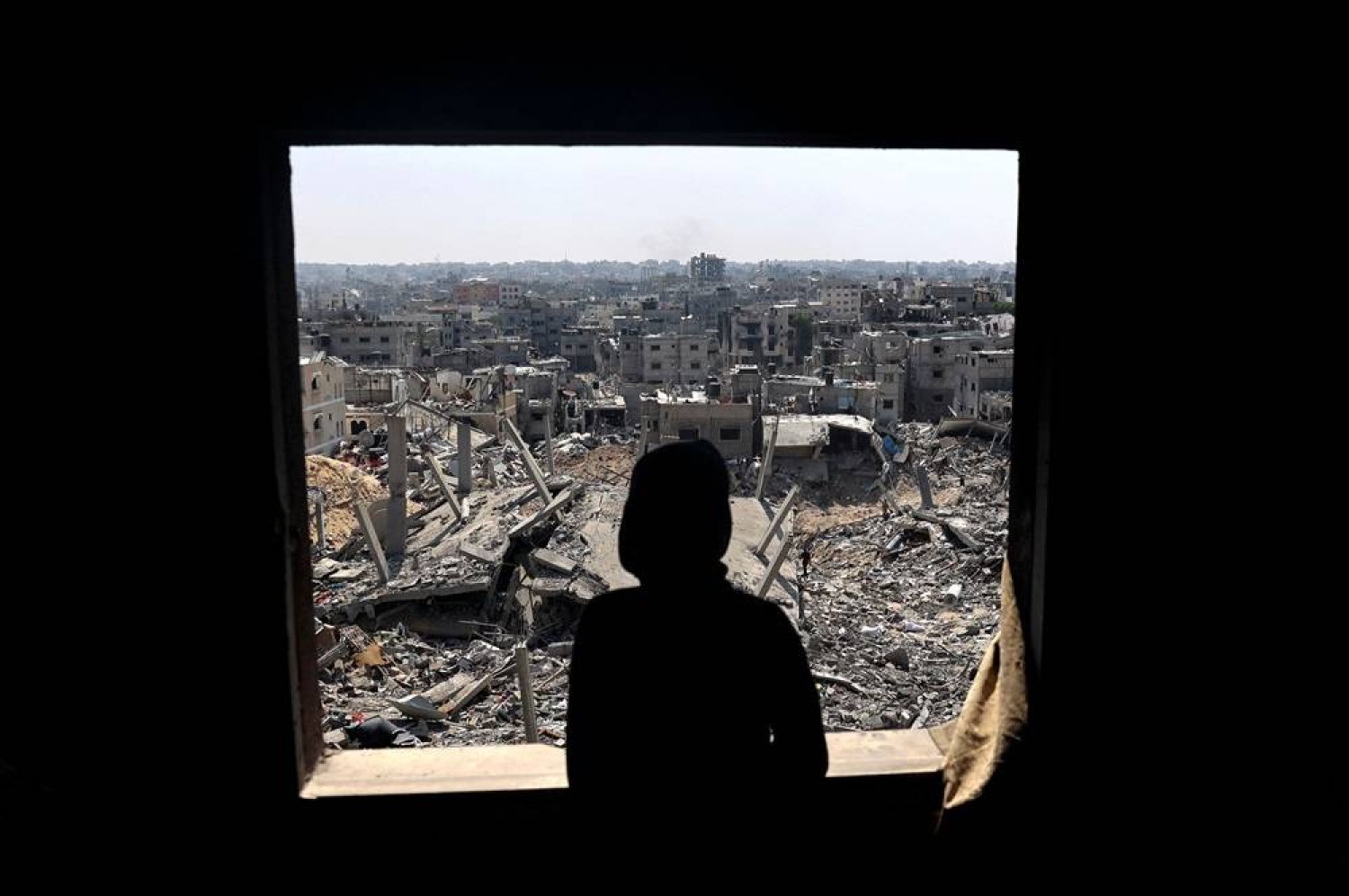 A Palestinian youth looks out of a window at buildings destroyed during Israeli bombardment in Khan Younis, on the southern Gaza Strip on April 16, 2024, as fighting continues between Israel and Hamas. (AFP) 
