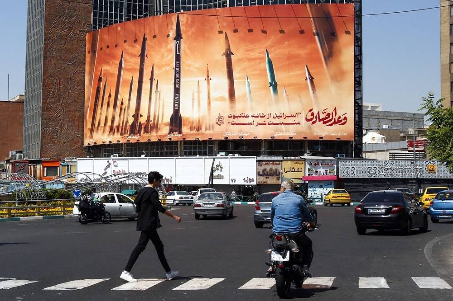 A man crosses a street as motorists drive past a billboard depicting Iranian ballistic missiles in service in Tehran on April 19, 2024. (AFP)