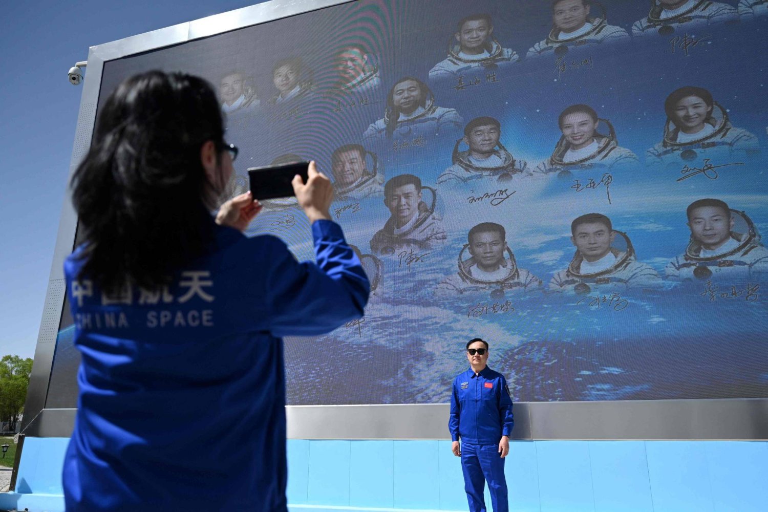A staff member poses for photos in front of a board featuring China's astronauts, after a press conference ahead of the Shenzhou-18 space mission, at the Jiuquan Satellite Launch Centre in the Gobi desert, in northwest China on April 24, 2024. (Photo by GREG BAKER / AFP)