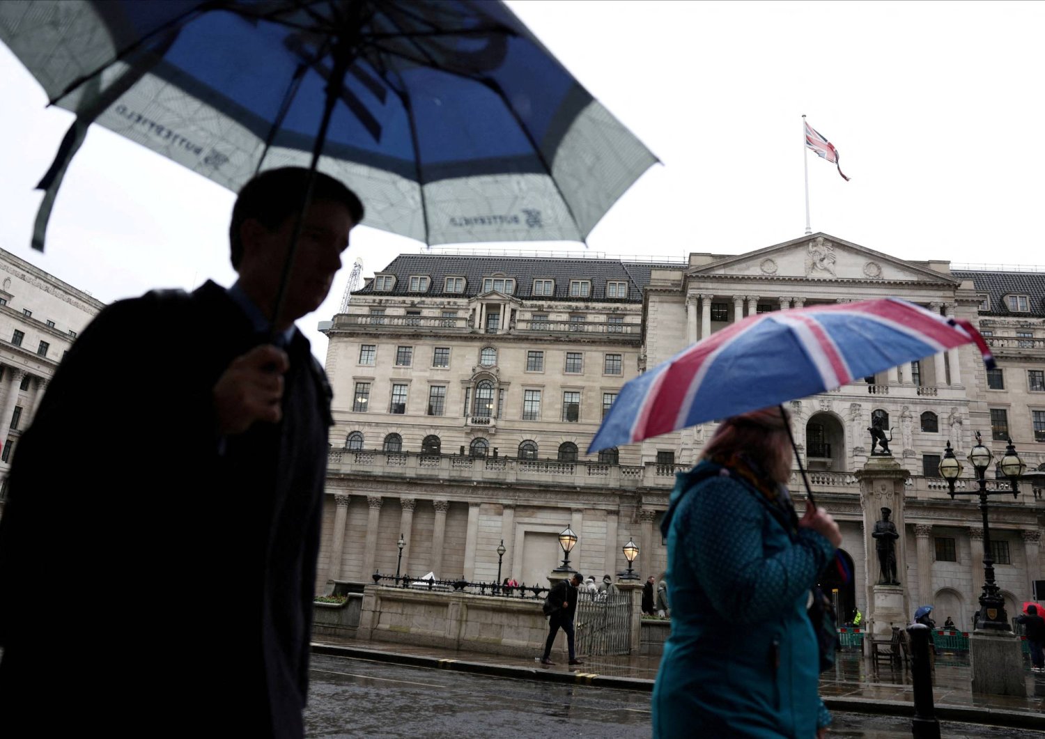 FILE PHOTO: A tourist shelters from the rain under an Union Jack umbrella near the Bank of England in the City of London financial district in London, Britain, February 13, 2024. REUTERS/Isabel Infantes/File Photo