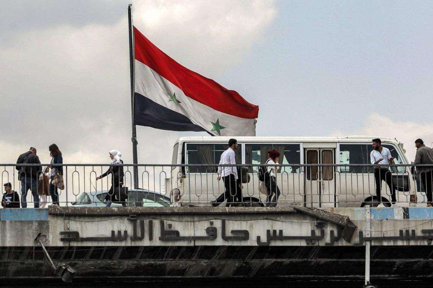 A Syrian flag flies as people walk across the Hafez al-Assad bridge across the Barada river in the center of Damascus on April 14, 2024. (AFP)