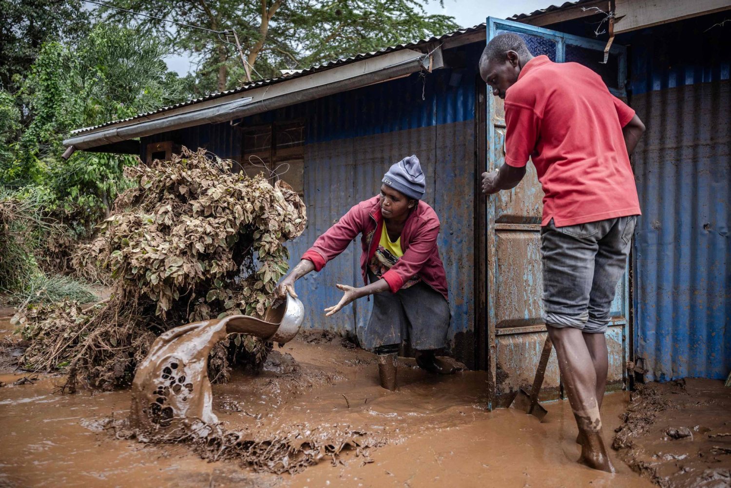 A woman and a man take mud and water out of their house in an area heavily affected by torrential rains and flash floods in Mai Mahiu, on April 29, 2024. (Photo by LUIS TATO / AFP)
