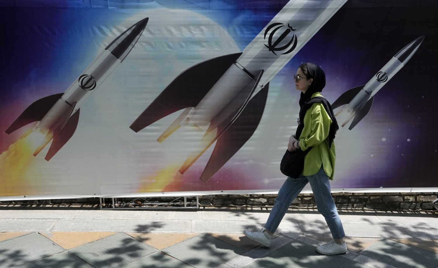 A woman walks past a banner showing missiles being launched, in northern Tehran, Iran, Friday, April 19, 2024. (AP) 