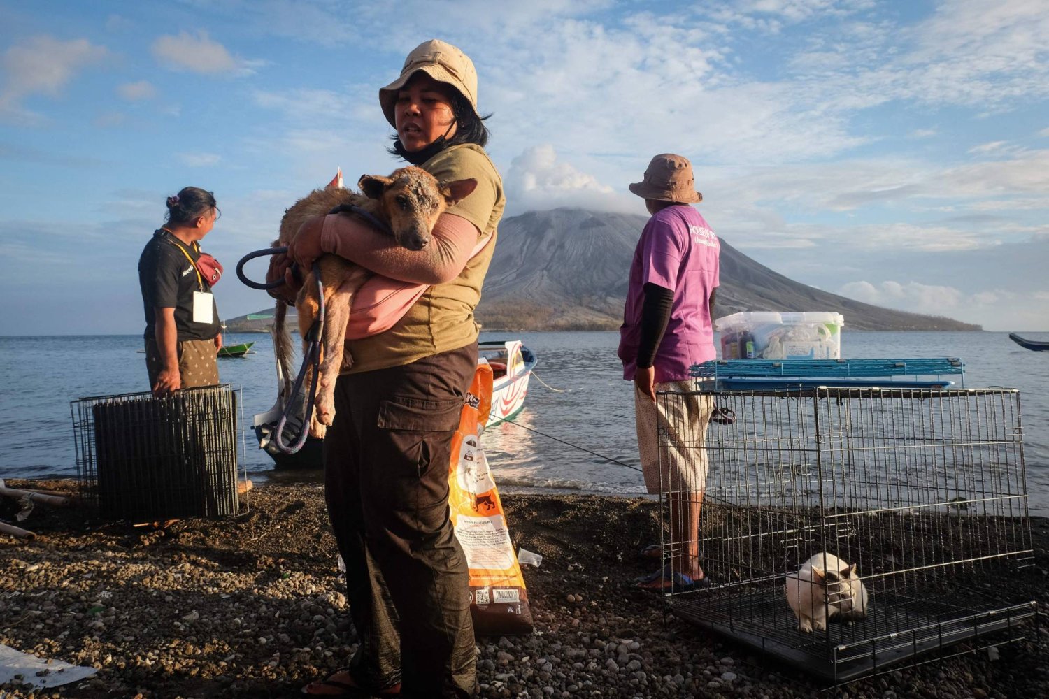 A volunteer carries a wounded dog as they bring back animals from the abandoned area at the foot of Mount Ruang volcano (background) on Tagulandang Island in Sitaro, North Sulawesi, on May 4, 2024. (Photo by Ronny Adolof BUOL / AFP)